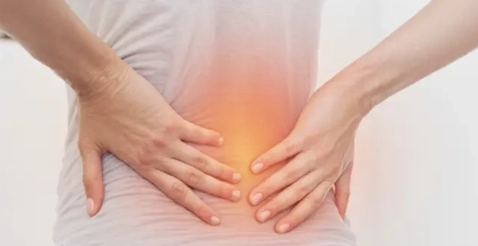 A person holding their lower back with both hands, indicating pain, and a red glow illustrating discomfort in the area.