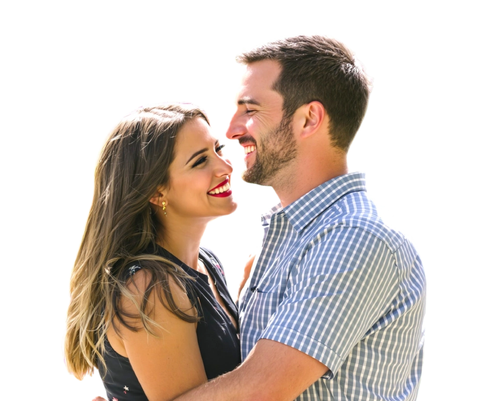 A couple stands closely, smiling at each other. The woman has long hair and is wearing a dark top, while the man has short hair and a checkered shirt.